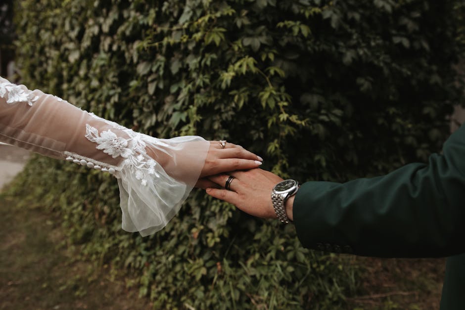 Beautiful close-up of bride and groom holding hands outdoors with lush greenery background.